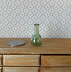 1:12 scale miniature real glass vase decanter in green with a long neck, shown on a wood dresser beside a coin