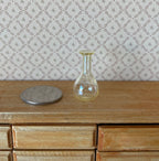 1:12 scale miniature clear glass decanter vase with round base and flared neck, shown on a wood dresser beside a coin