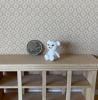 1:12 scale miniature sitting bear figurine in white with blue eyes, shown on a wood shelf beside a coin for scale