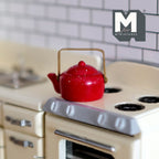 1:12 scale miniature enamel kettle in red with white speckles, gold handle and fixed lid, on a cream stove