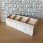 1:12 scale miniature unpainted wood produce display shelf with 4 sections, slanted bins shown against a stone wall