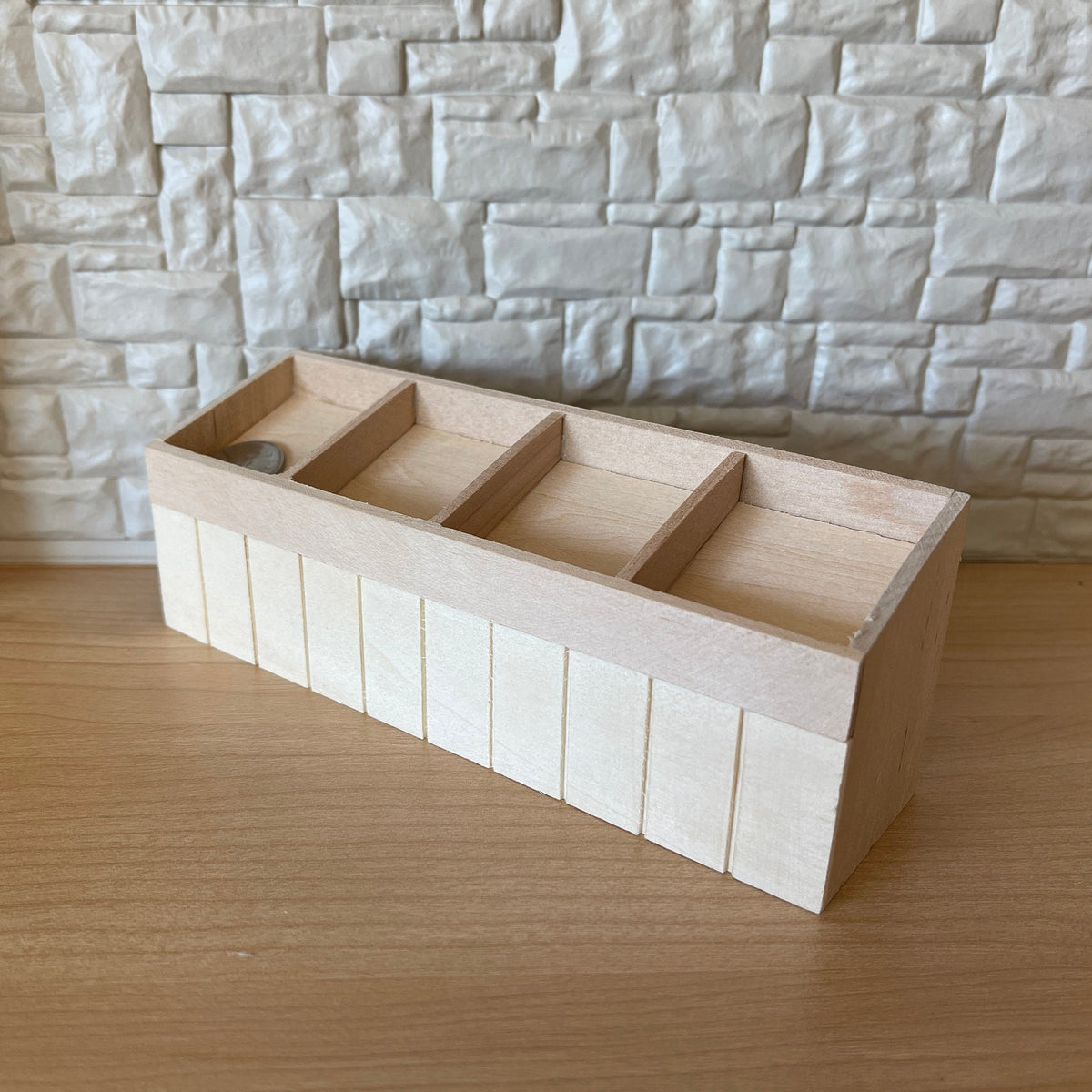 1:12 scale miniature unpainted wood produce display shelf with 4 sections, slanted bins shown against a stone wall