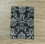 1:12 scale miniature damask area rug in black and white with woven floral scroll pattern, on a wood floor