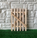 1:12 scale miniature picket gate panel with diagonal brace in unfinished wood, ready to paint, standing on green turf
