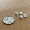 1:12 scale miniature white ceramic door knobs, set of 4, shown on a wood surface beside a coin for scale