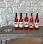 1:6 scale miniature red wine bottles with assorted labels, set of 5, shown in a row on a table beside a coin