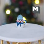 1:12 scale miniature Christmas snowman mug with lid in white with a blue hat and scarf, shown on a white table