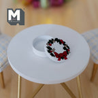 1:12 scale miniature round Christmas tin in white with a holly wreath and red bow lid, shown open on a white table