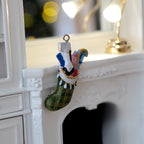 1:12 scale miniature cast resin filled Christmas stocking in green with hanging loop, shown hung on a white fireplace