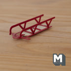 1:12 scale miniature metal sledge in red with wood base and curved runners, shown on a wood surface