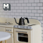 1:12 scale miniature black metal gooseneck coffee drip kettle, shown on a cream stove in a tiled kitchen