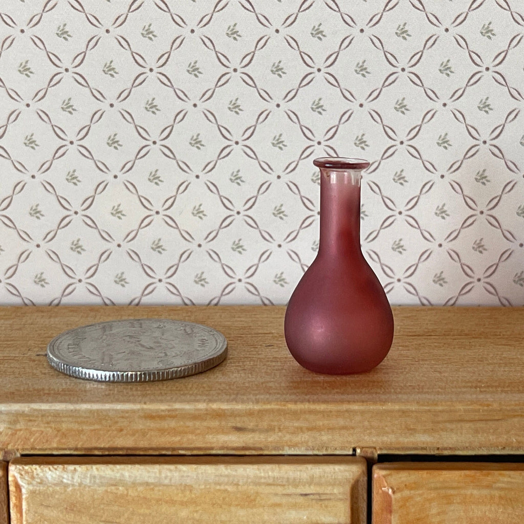 1:12 scale miniature glass decanter vase in dark red with a long neck, shown on a wood dresser beside a coin