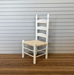 1:12 scale miniature white ladder back dining chair with natural woven seat, shown on a dark wood floor