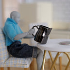 1:12 scale miniature metal jug with handle and lid in chromed black, shown held by a poseable figure at a table