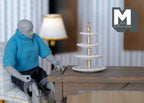 1:12 scale miniature 4 tier dessert stand in white with round tiers and gold center post, on a table by an artist figure