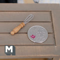 1:12 scale miniature wire whisk with turned wood handle, shown on a gray wood table beside a coin for scale