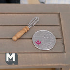 1:12 scale miniature wire whisk with turned wood handle, shown on a gray wood table beside a coin for scale