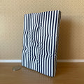 1:12 scale miniature striped double mattress in navy blue and white with tufting, shown leaning on a wall beside a coin