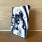 1:12 scale miniature striped double mattress in navy blue and white with tufting, shown leaning on a wall beside a coin