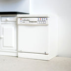 1:12 scale miniature white wood built in dishwasher with opening door and wire racks, beside a kitchen cabinet