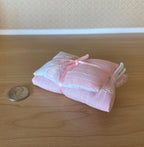 1:12 scale miniature single bedding set with pillow, comforter and sheet in pink, tied with ribbon, shown beside a coin