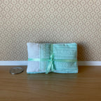 1:12 scale miniature single bedding set in mint green with pillow, comforter and cover sheet, tied with ribbon beside a coin