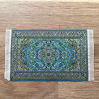1:12 scale miniature woven medallion area rug with white fringe in teal blue with a floral border, shown on a wood floor