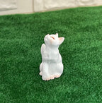 1:12 scale miniature resin sitting cat in white, looking up with pink ears, shown on green grass