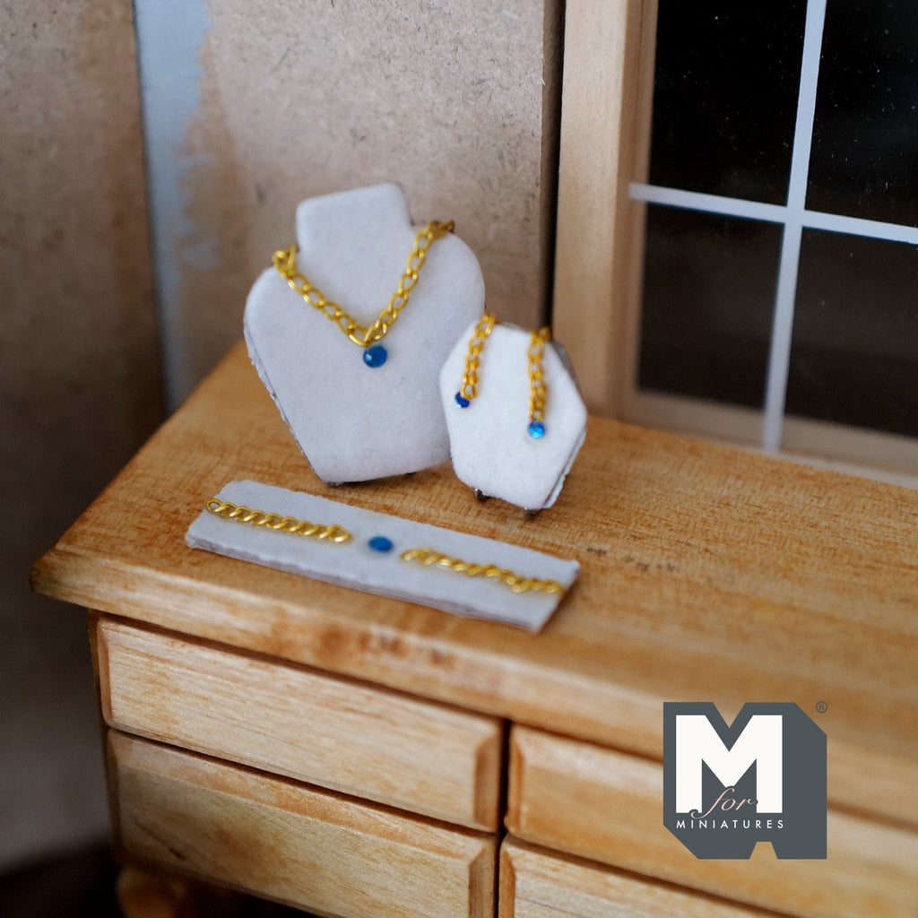 1:12 scale miniature jewelry set on stands in blue, necklace, earrings and bracelet with gold chain, on a wood dresser