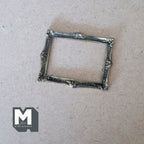 1:12 scale miniature metal ornate picture frame in antique silver with scroll corners, lying on a tan surface