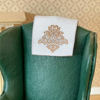 1:12 scale miniature chair antimacassars in white with a gold damask motif, set of 2, one draped on a green armchair