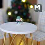 1:12 scale miniature ceramic Christmas snowman mug with green hat and scarf, on a white round table by a Christmas tree