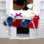1:12 scale miniature Christmas stockings in navy blue and red with bows and lace trim, set of 4, hung on a white fireplace
