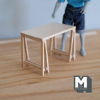 1:12 scale miniature unpainted wood trestle table with plank top and A frame legs, shown beside a figure for scale