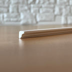 Miniature slim wood trim molding in white for cornices and picture rails, close up of the profile on a wood floor