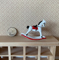 1:12 scale miniature metal rocking horse in white with red saddle and black mane, shown on a wood shelf beside a coin