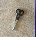 1:12 scale miniature sewing scissors with black handles and silver blades, shown on a beige surface