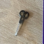 1:12 scale miniature sewing scissors with black handles and silver blades, shown on a beige surface