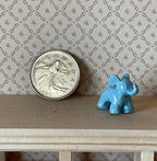 1:12 scale miniature light blue toy elephant figurine with raised trunk, shown on a shelf beside a coin for scale
