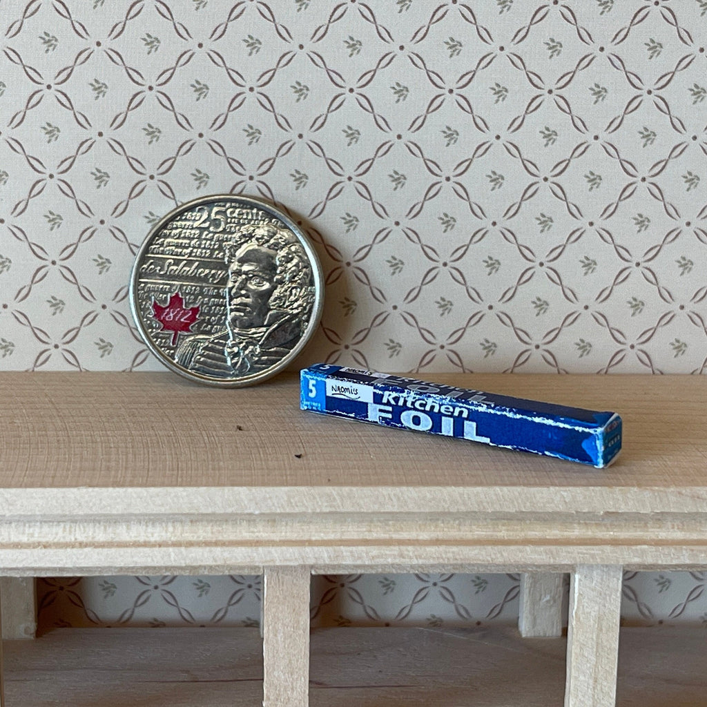 1:12 scale miniature blue kitchen foil box, box only, shown on a wood shelf beside a coin for scale