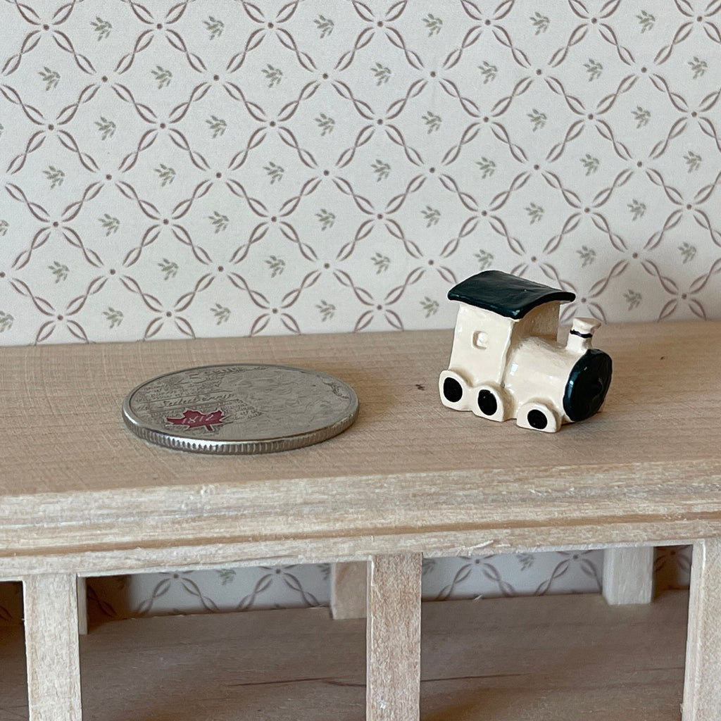 1:12 scale miniature cast resin toy locomotive in white and black, shown on a wood shelf beside a coin for scale