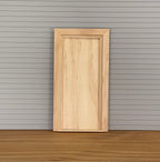 1:12 scale miniature unfinished wood plain interior door with back trim, shown against gray siding on a wood floor