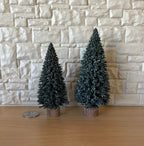 1:12 scale miniature evergreen trees with wood bases in green, set of 2, shown against a stone wall beside a coin