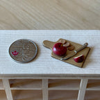 1:12 scale miniature round red cheese with crackers and knife fixed to a wood cutting board, beside a coin for scale