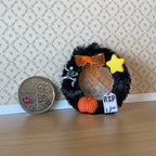 1:12 scale miniature black Halloween wreath with pumpkins, tombstone, star and orange bow, shown beside a coin