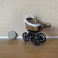 1:12 scale miniature wicker style baby pram with white lace hood and black metal frame, shown beside a coin for scale