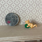1:12 scale miniature orange kitten playing with a green yarn ball, on a wood shelf beside a coin for scale