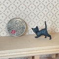 1:12 scale miniature black walking kitten figure with raised tail, shown on a wood shelf beside a coin for scale