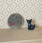 1:12 scale miniature sitting kitten in black with raised tail, shown on a wood shelf beside a coin for scale