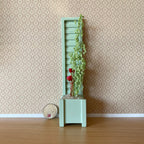 1:12 scale miniature mint green wood planter box with trellis back and climbing flowers, shown beside a coin